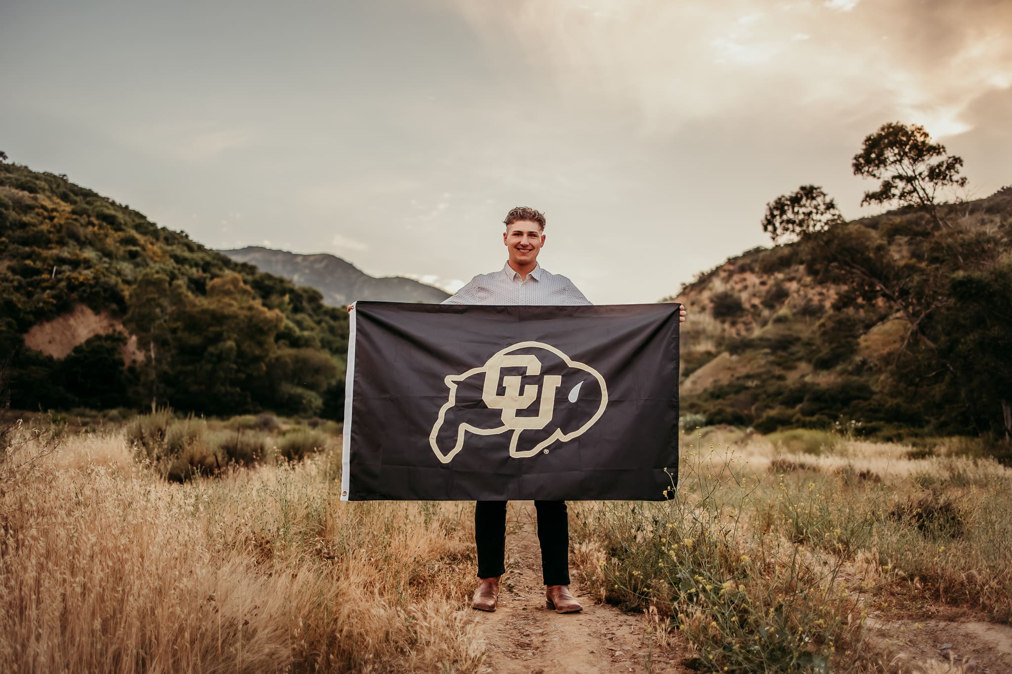 High school senior boy holding Colorado Buffaloes college flag during golden hour photo session in Corona California