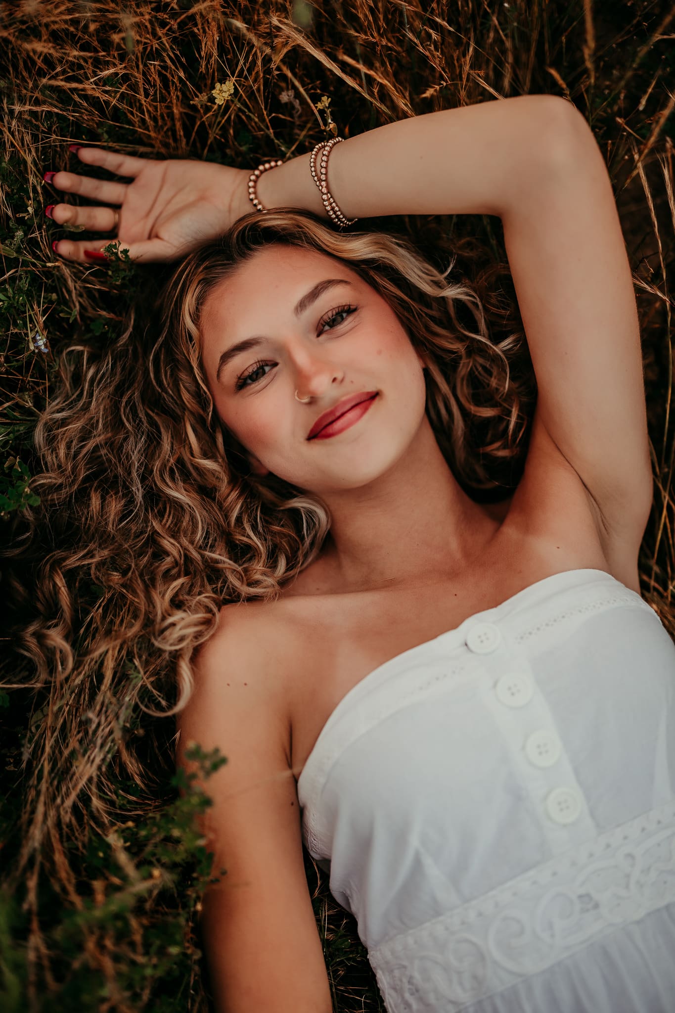 High school senior girl with curly hair lying in grass during golden hour photo session in Corona California