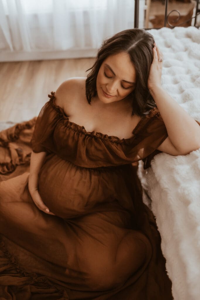 Expecting mother relaxing on a couch during a maternity photography session near Corona, CA, captured indoors with soft natural light and a warm, lifestyle feel.
