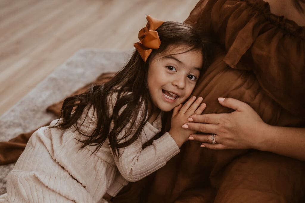 big sister putting her ear up to her expecting moms belly, listening for baby sister.