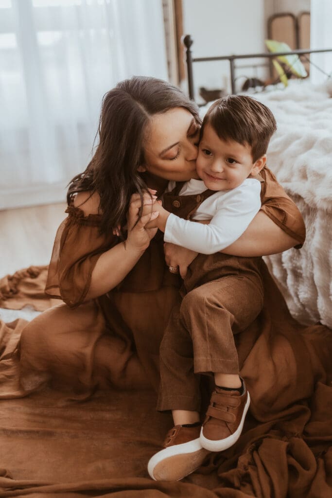 Mother cuddling her toddler during an indoor maternity photography session near Corona, California, captured in a relaxed, natural light studio setting