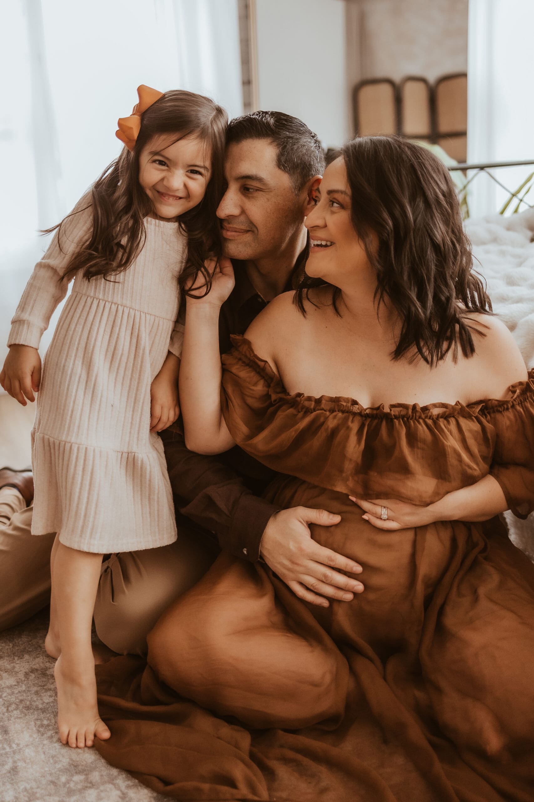 Family cuddling together during an indoor maternity photography session near Corona, CA, capturing a joyful, lifestyle moment with parents and their young daughter