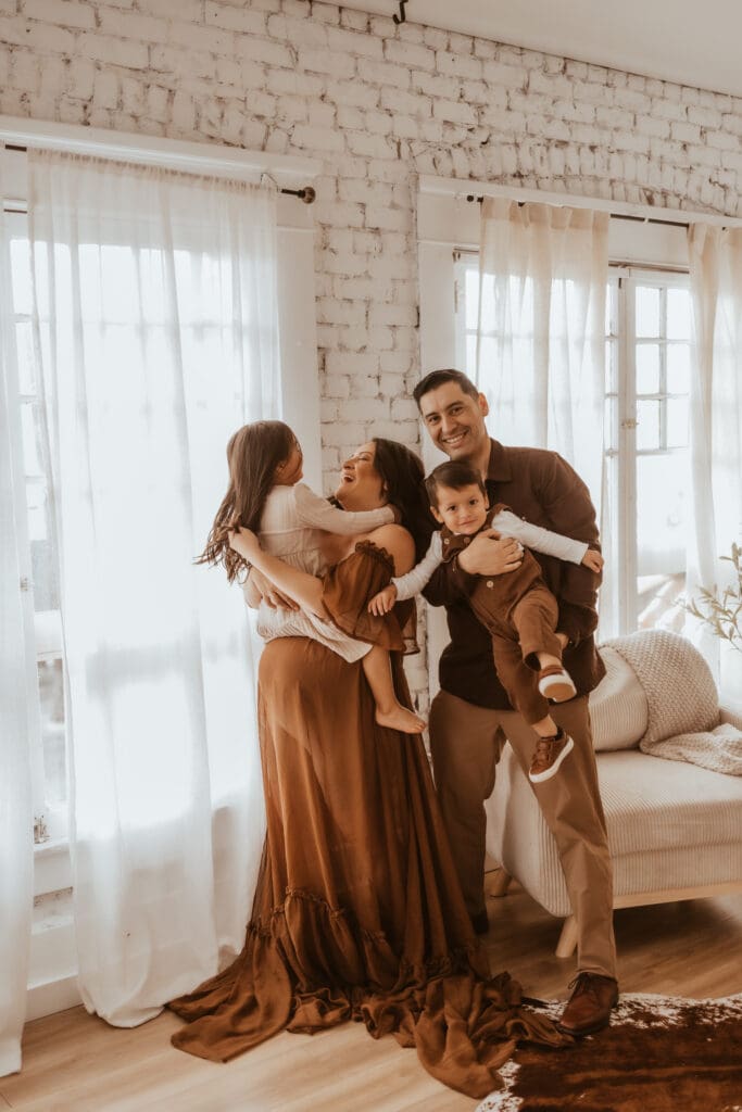 Family embracing during a maternity photography session near Corona, CA, photographed indoors with natural light and a warm, lifestyle feel.