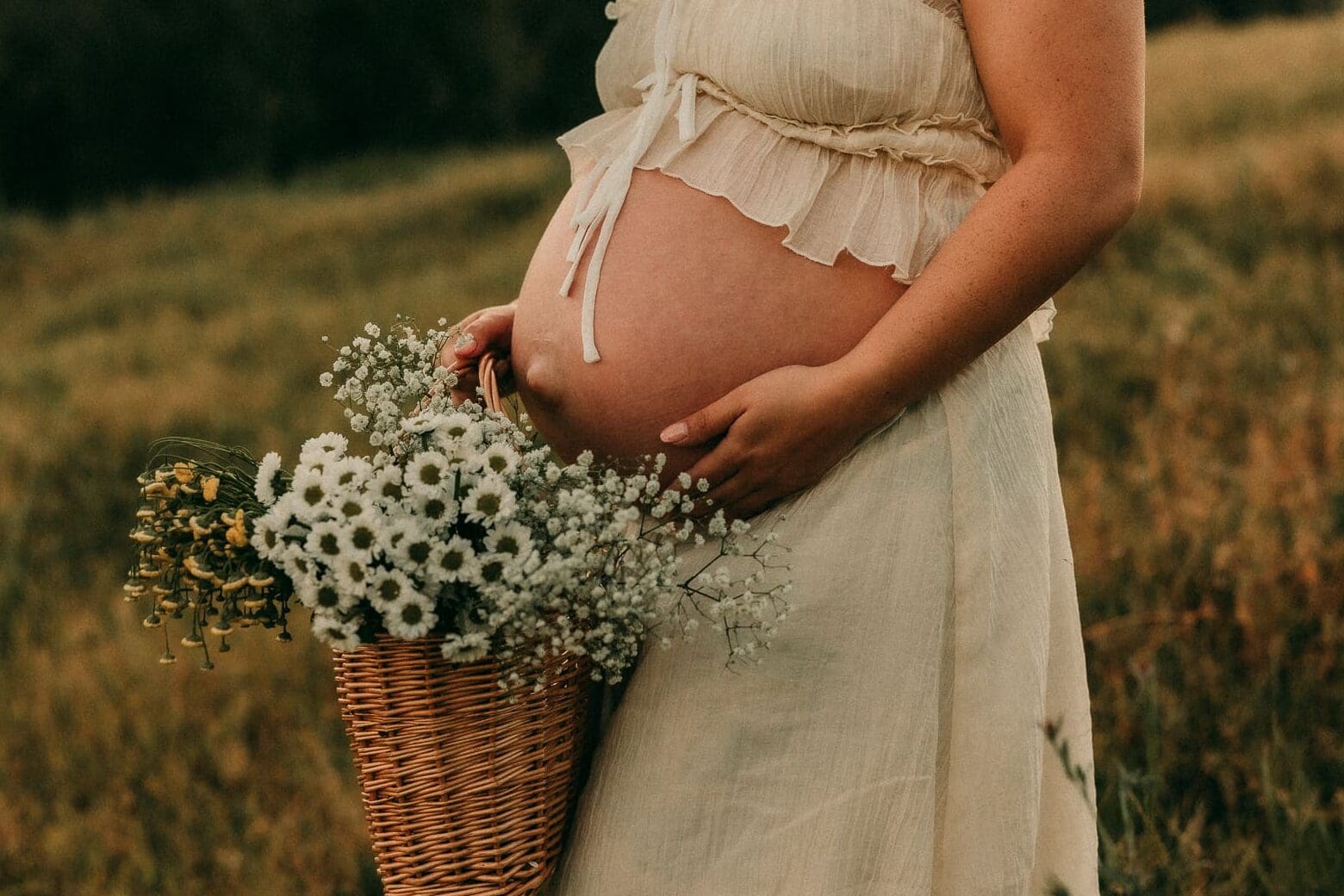 a close up of a pregnant woman's belly with a basket of flowers near by at golden hour