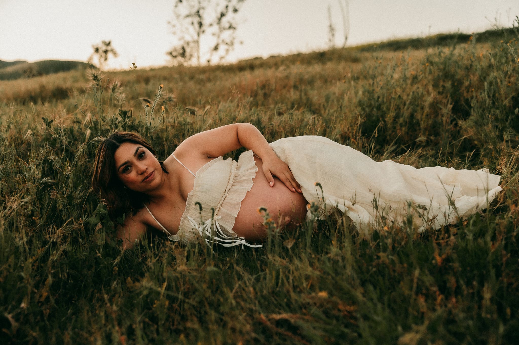 Pregnant woman laying in the grass holding her belly in Chino Hills